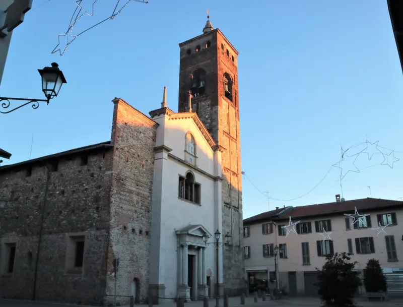 La collegiata di Santo Stefano al tramonto: facciata bianca con portale a colonne, fianco in ciottoli e mattoni e il campanile medievale in mattoni