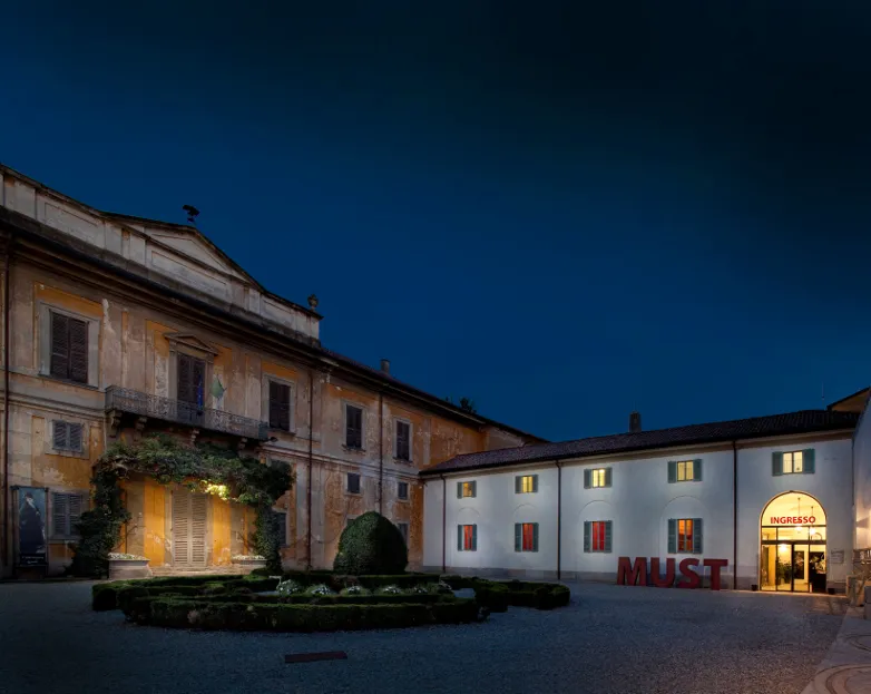La corte di Villa Sottocasa di sera, con il parterre e l’ingresso illuminato del MUST